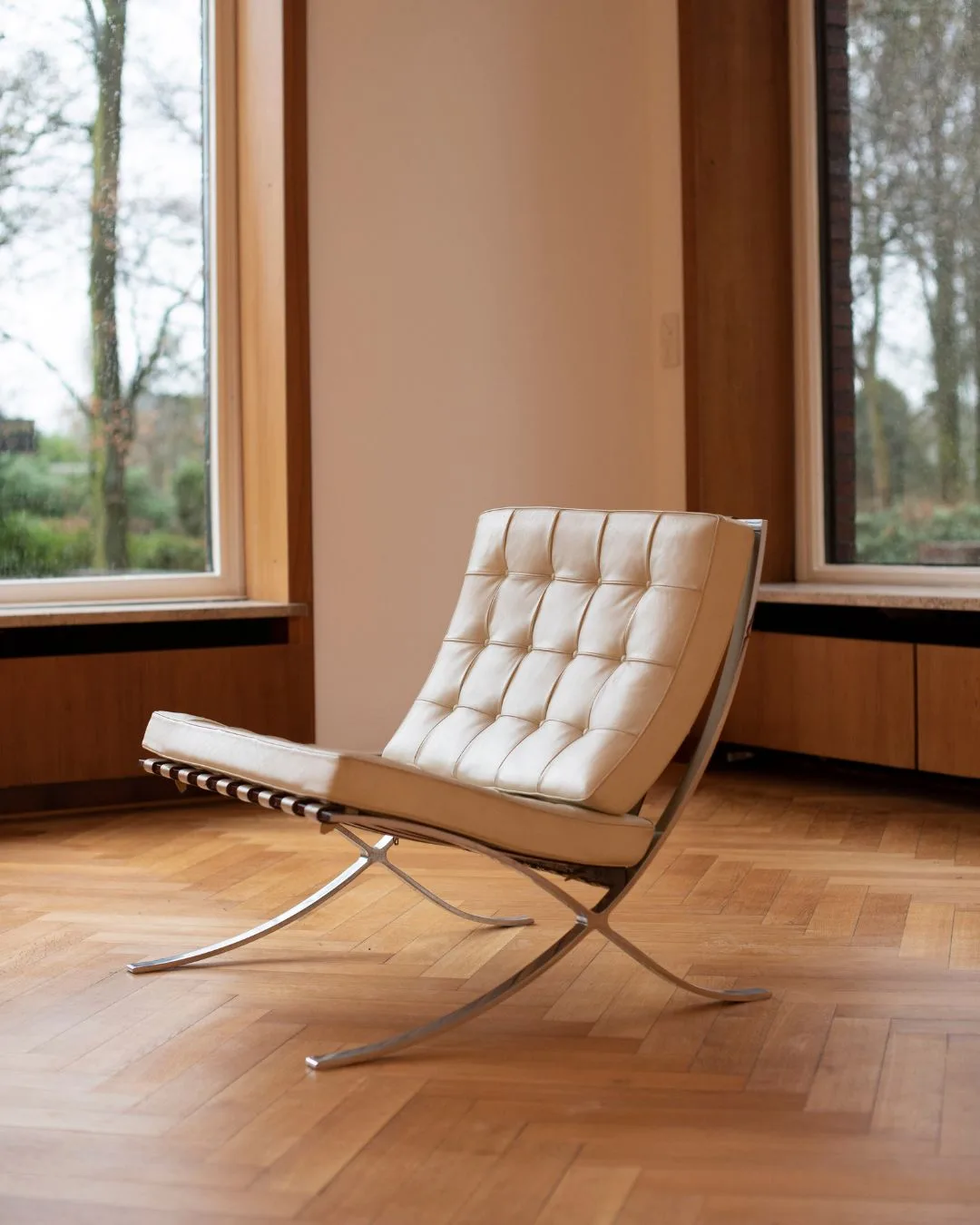 A lone white Barcelona Chair sits in a room with timber hardwood floors 