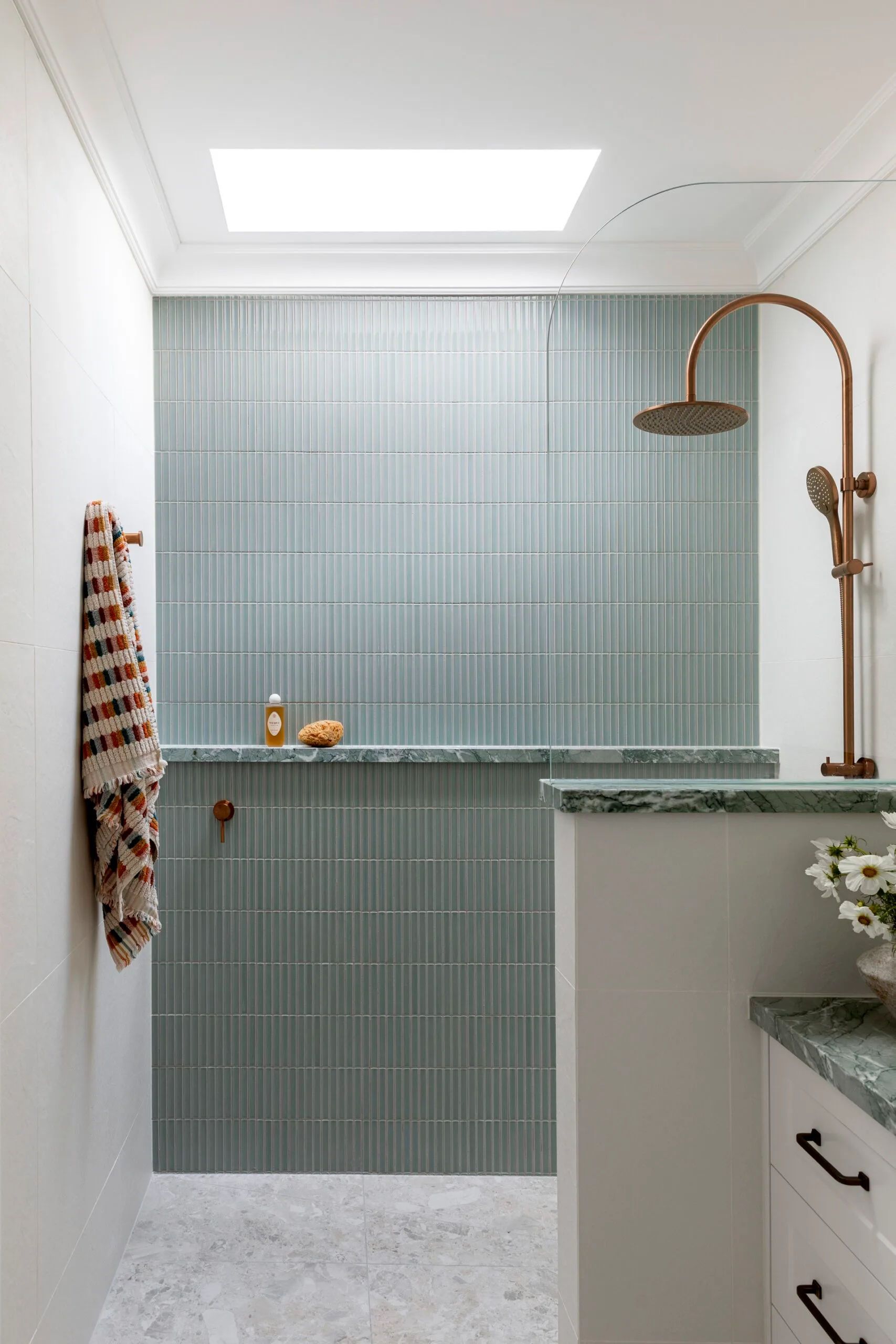 Bathroom in a Cape Cod style home, with skylight, blue wall tiles, copper shower, and colorful towel on a peg.