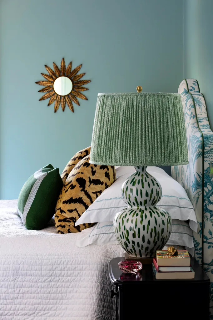 Bedroom with a patterned lamp, pillows, and decorative sunburst mirror on a teal wall.