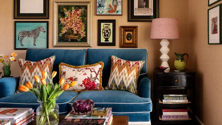 Living room with a blue sofa, colorful cushions, a gallery wall of art, side table with lamp, and tulip vase.