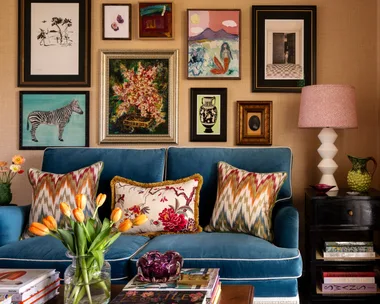 Living room with a blue sofa, colorful cushions, a gallery wall of art, side table with lamp, and tulip vase.