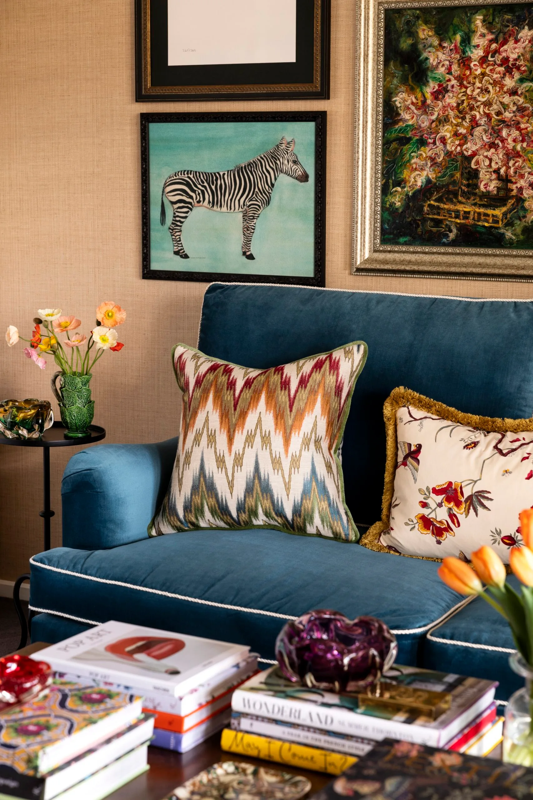 Cozy living room with blue velvet chair, patterned pillows, zebra artwork, and books on table.