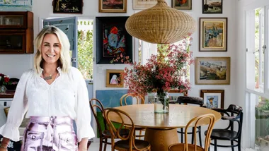 Headshot of Julia Green with no background. This is placed in front of a photo of a cottage style dining area with a powder blue door, white walls, round timber dining table and chairs plus large rattan pendant hanging above. The white walls are covered in art, in different frames and depicting various landscapes, flowers and birds. The gallery wall is eclectic yet cohesive.