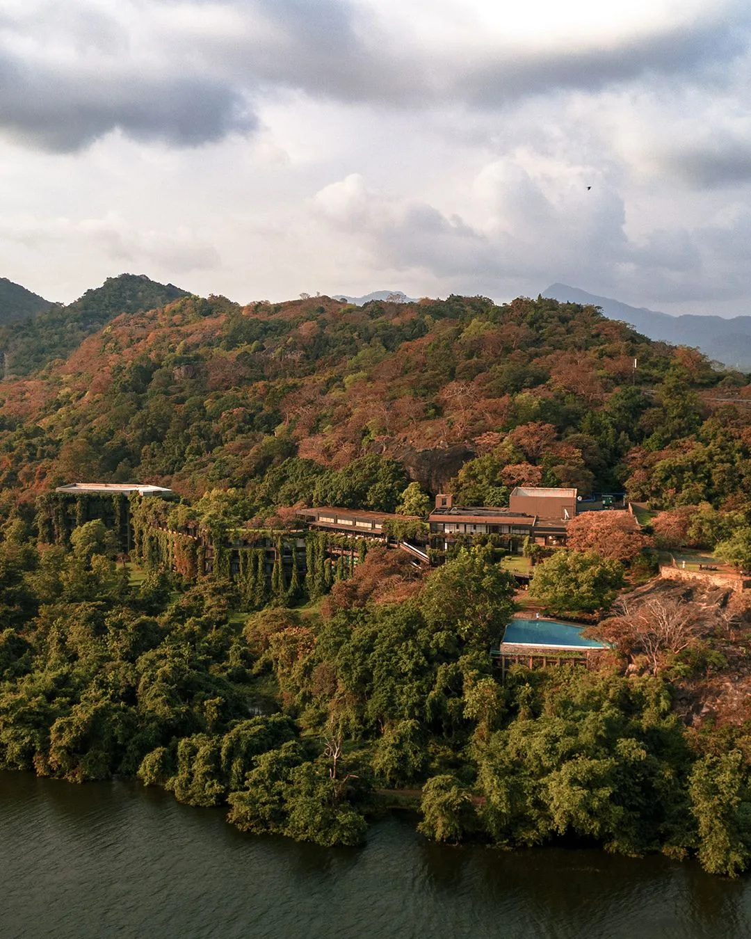 a far away view of Tropical Modernist Kandalama hotel in Sri Lanka by architect Geoffrey Bawa, built into a mountain side and covered by jungle