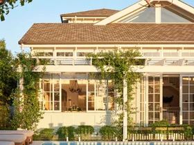 White house with large windows, greenery, and a pool reflecting the building against a clear blue sky.
