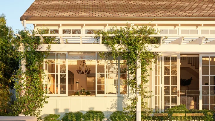 White house with large windows, greenery, and a pool reflecting the building against a clear blue sky.