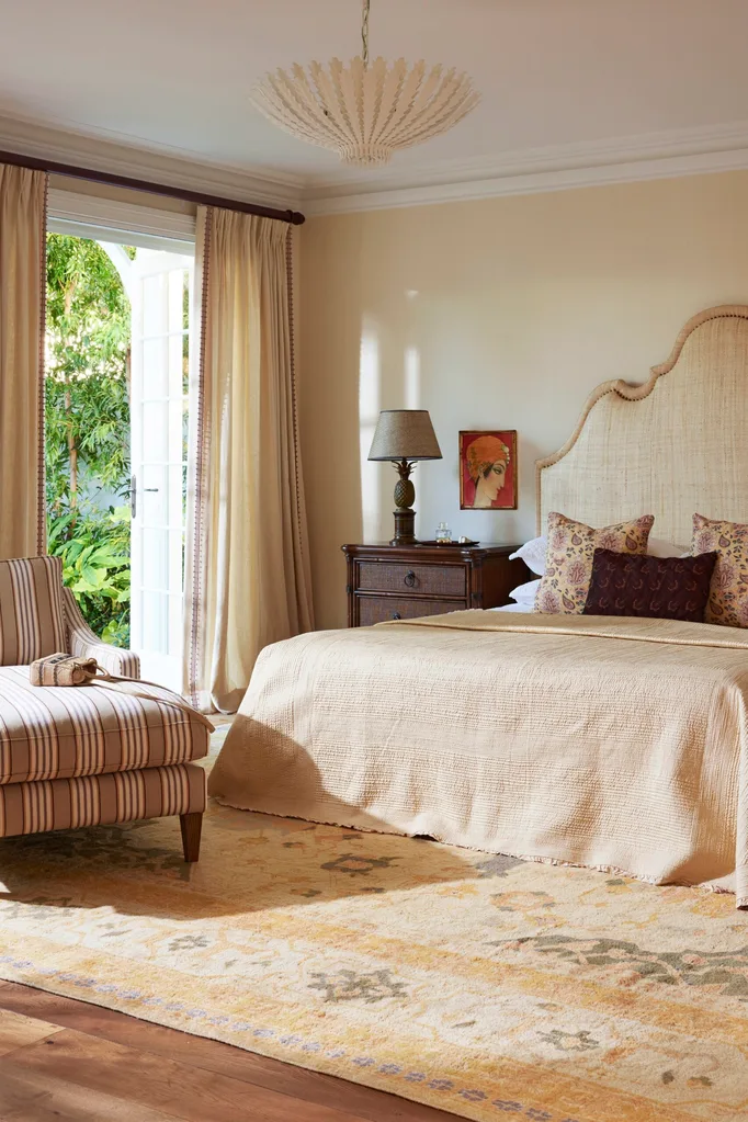 Elegant bedroom with a beige theme, featuring a cozy bed, patterned cushions, a striped chair, and ample natural light.