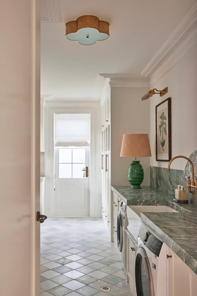 Laundry room with marble countertops, washing machines, green lamp, and window with light filtering in.