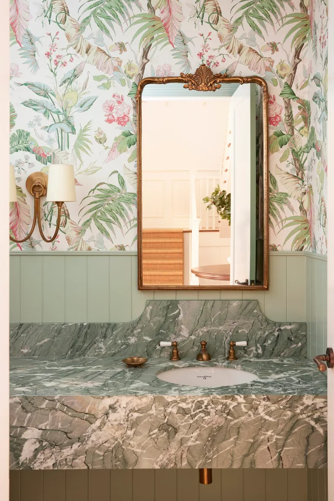 Elegant bathroom with floral wallpaper, gold-framed mirror, green marble countertop, and brass fixtures.