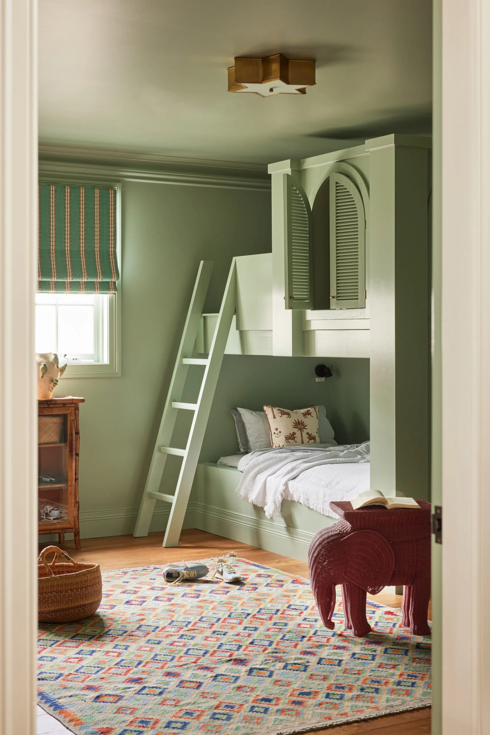 Green room with a bunk bed, ladder, patterned rug, and elephant-shaped side table.