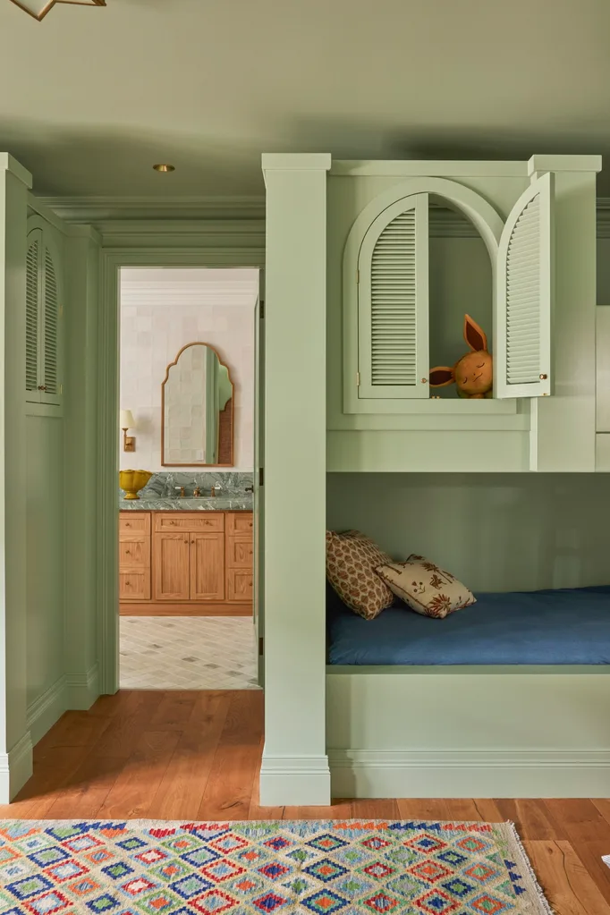 Green bunk bed room with open cabinet; colorful rug and a bathroom with wooden cabinetry in the background.