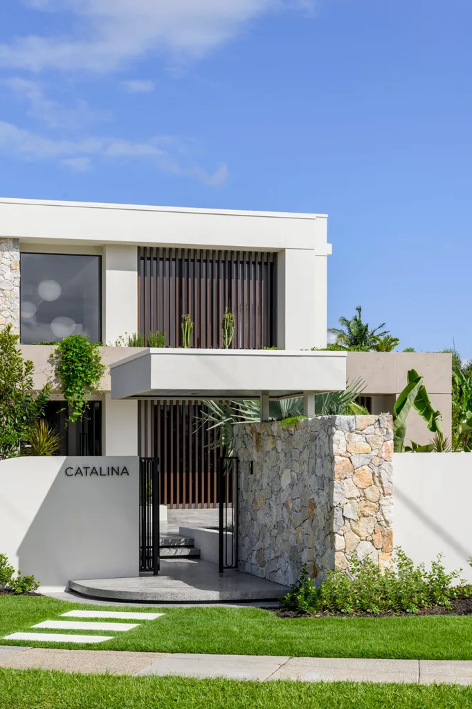 Modern two-story building with "CATALINA" sign, stone entrance, and lush greenery under a clear blue sky.