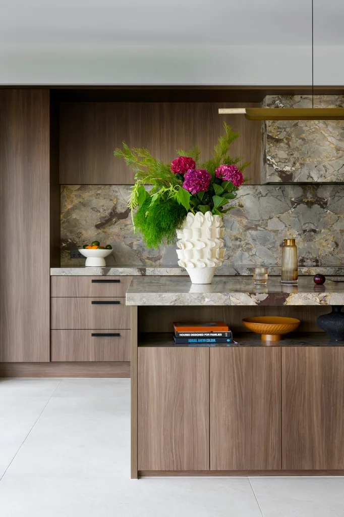 Modern kitchen with dark wood cabinets, marble backsplash, a vase with pink flowers, and books on the counter.