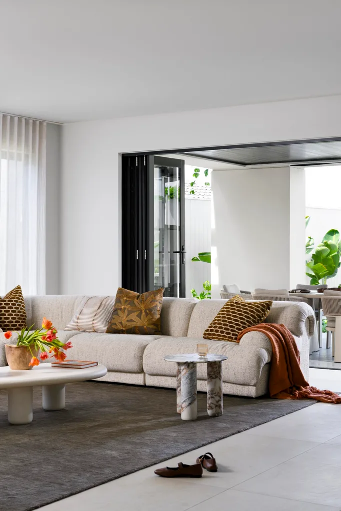 Luxurious living room with beige sofa, decorative cushions, and a coffee table with flowers. Bright and open space.