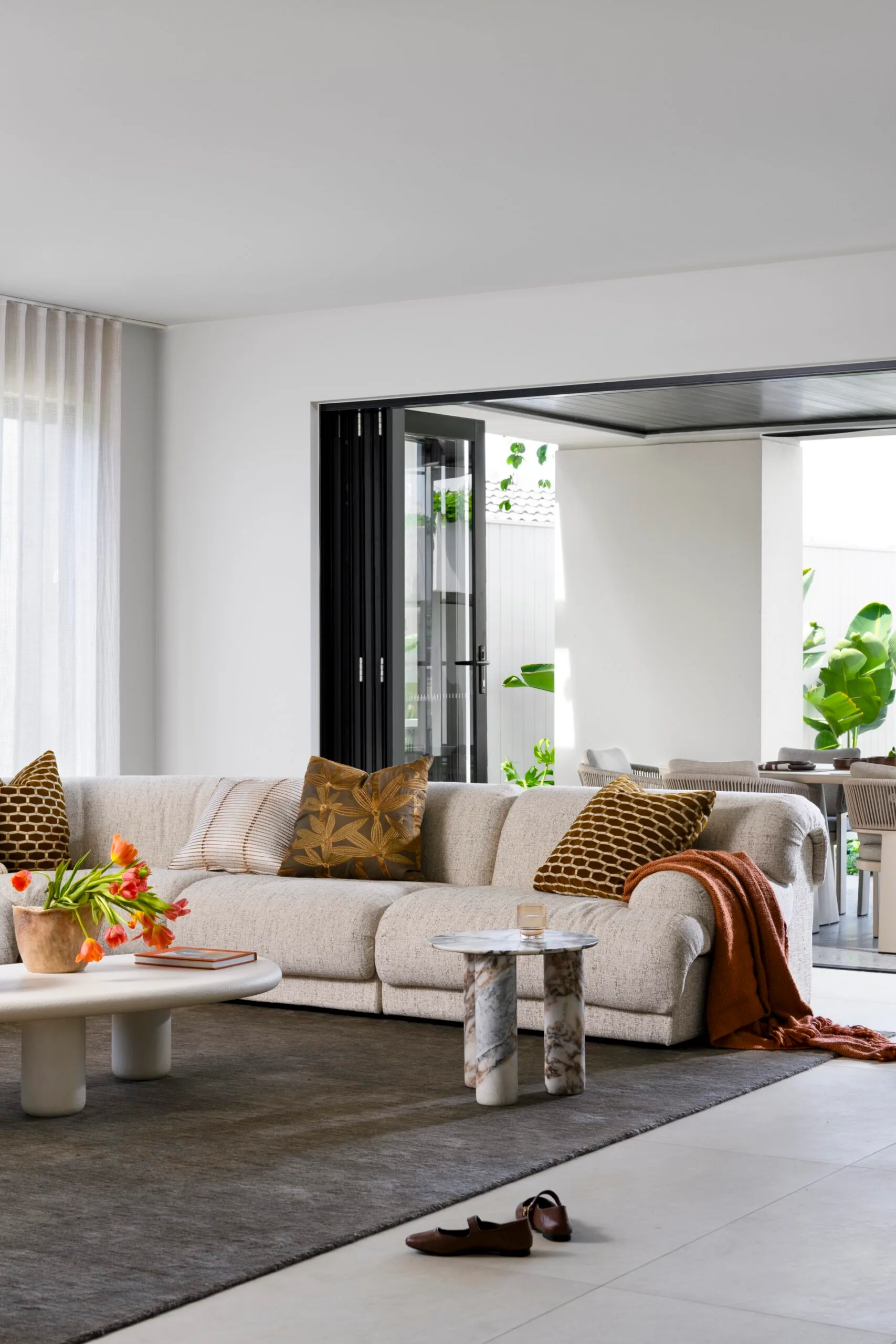 Luxurious living room with beige sofa, decorative cushions, and a coffee table with flowers. Bright and open space.