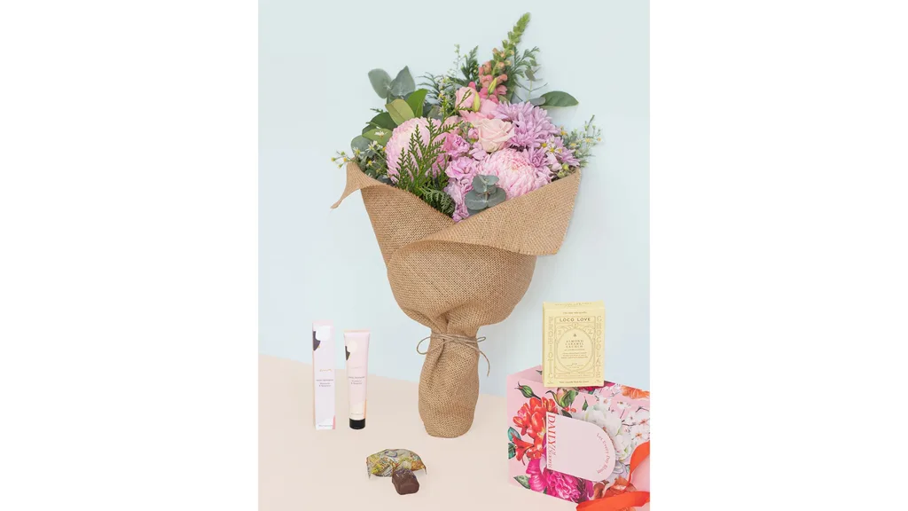 A bouquet of flowers with a few other small gifts around it, including hand cream and a chocolate.