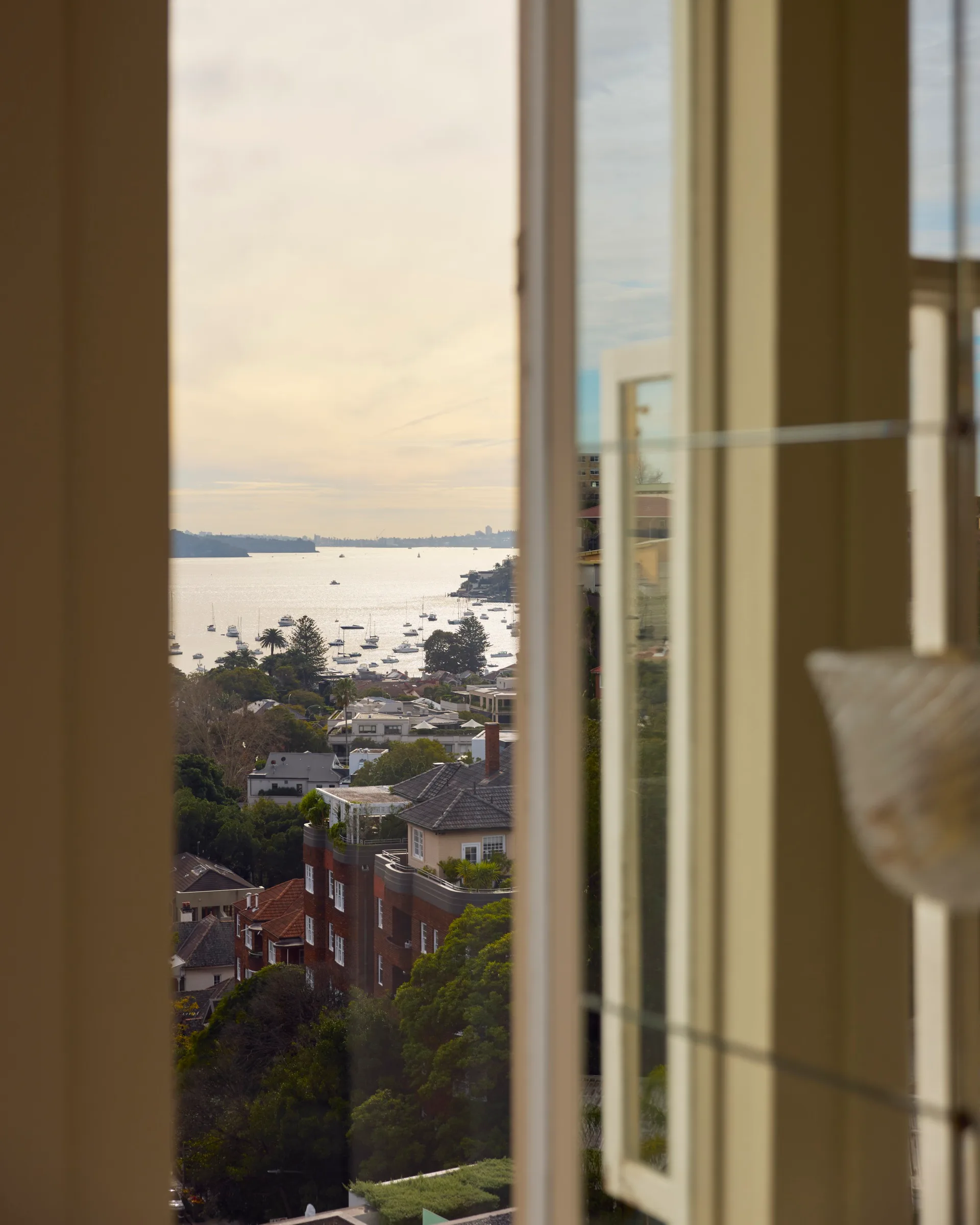 View through a window showing a coastal neighborhood with houses, trees, and boats on a calm water body.
