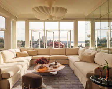 Cream sectional sofa in bright living room with cityscape view, wooden coffee table, and decorative ceiling light.