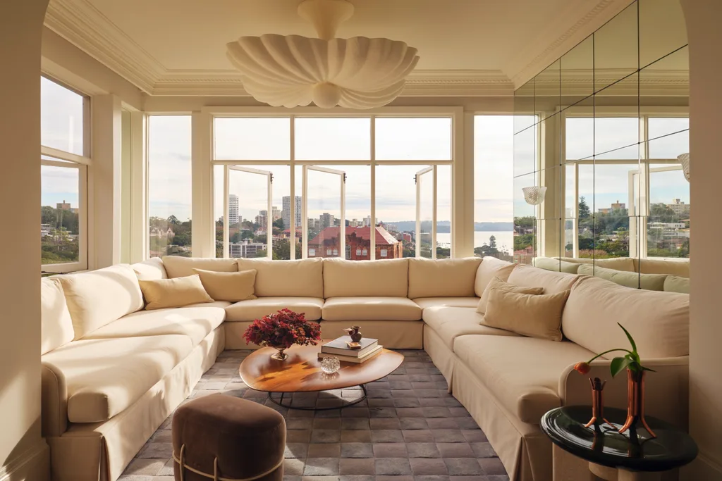 Cream sectional sofa in bright living room with cityscape view, wooden coffee table, and decorative ceiling light.