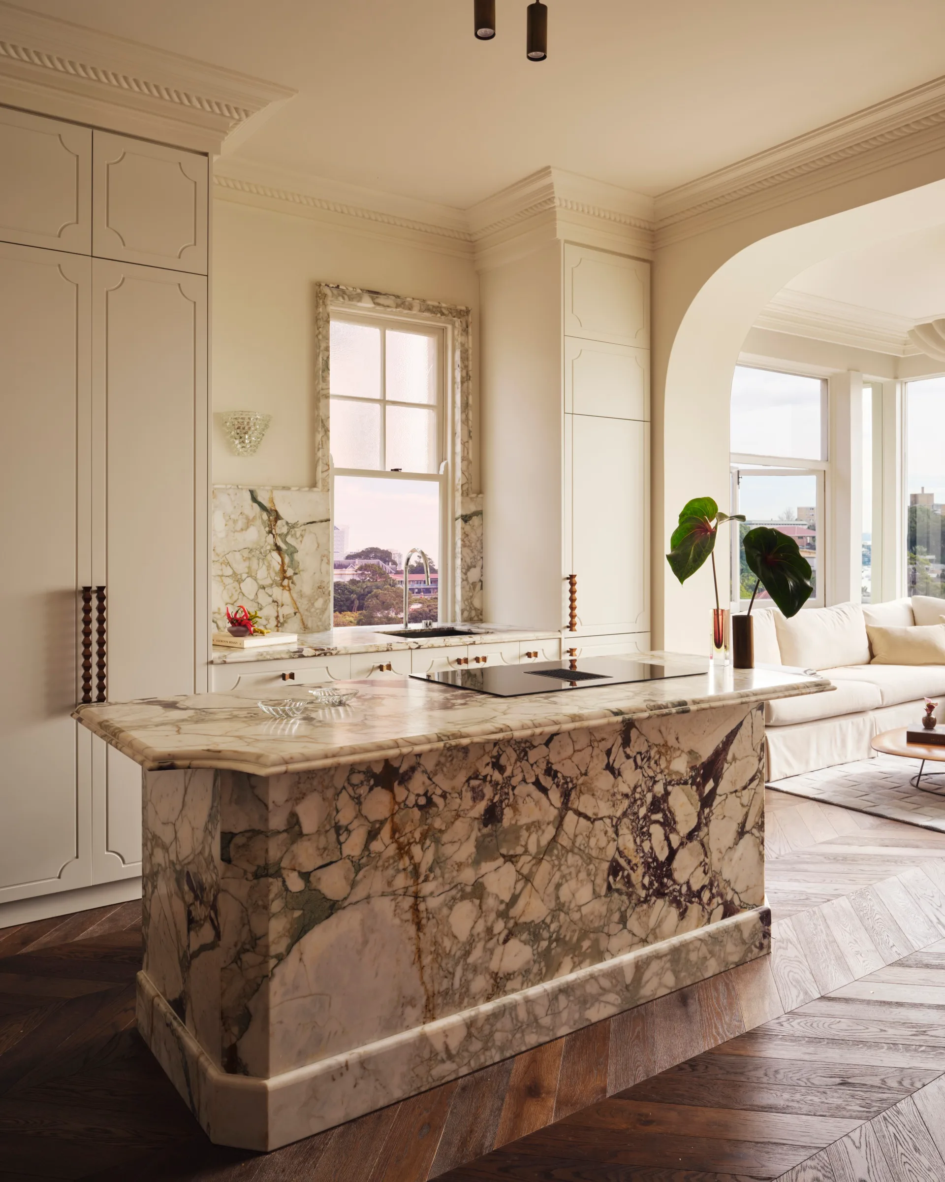 Elegant kitchen with marble island, large window, and plant in a modern, well-lit open plan living space.