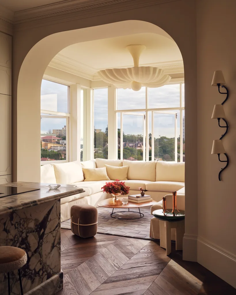 Elegant living room with a large beige sectional sofa, marble countertop, hardwood floor, and arched window view.