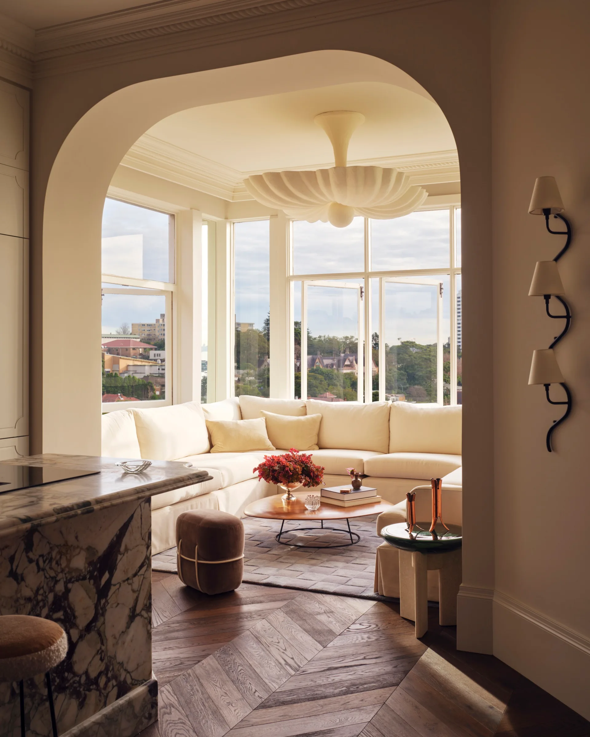 Elegant living room with a large beige sectional sofa, marble countertop, hardwood floor, and arched window view.