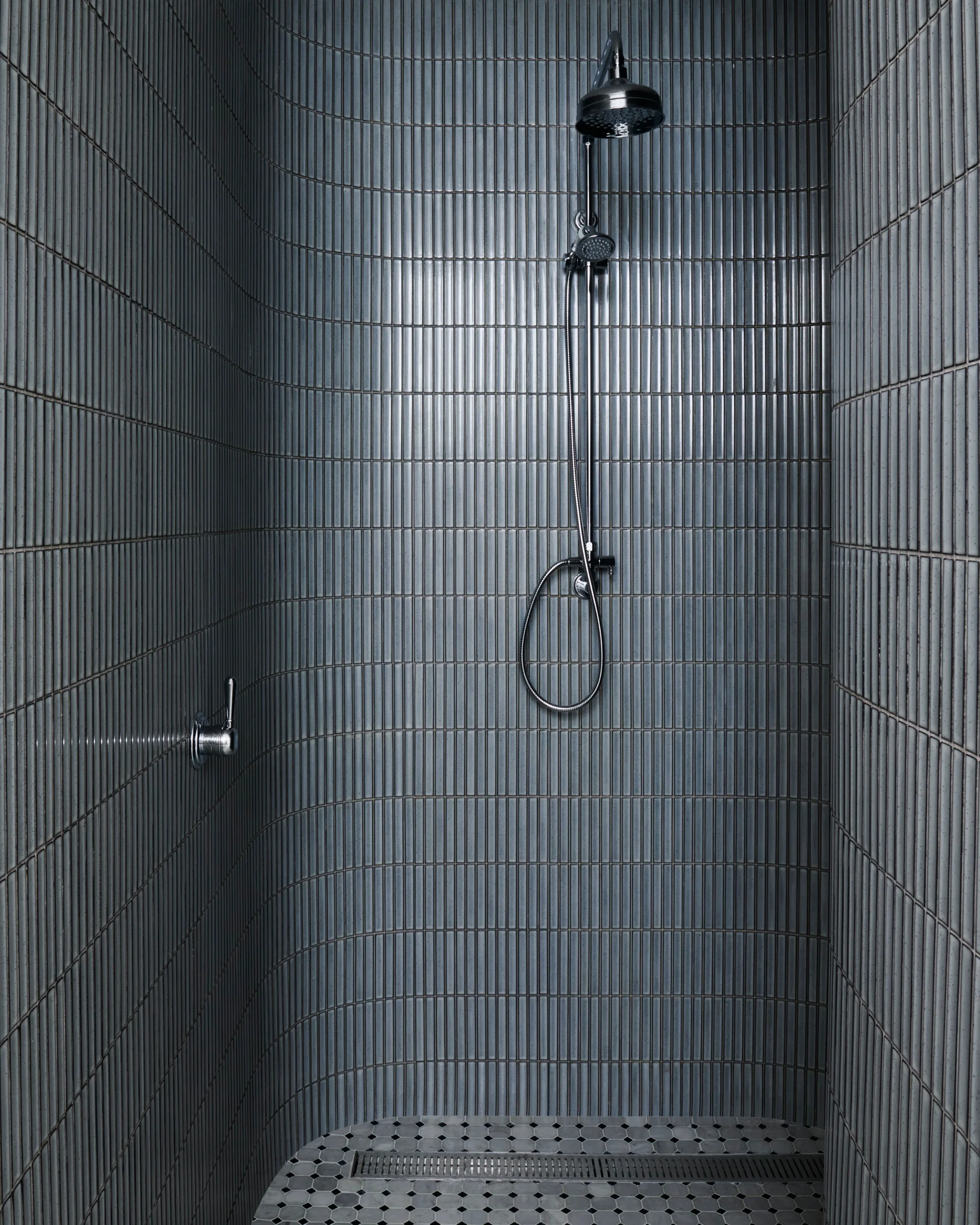 Modern shower with dark blue kit kat tiles, laid vertically, chrome showerhead and tapware.