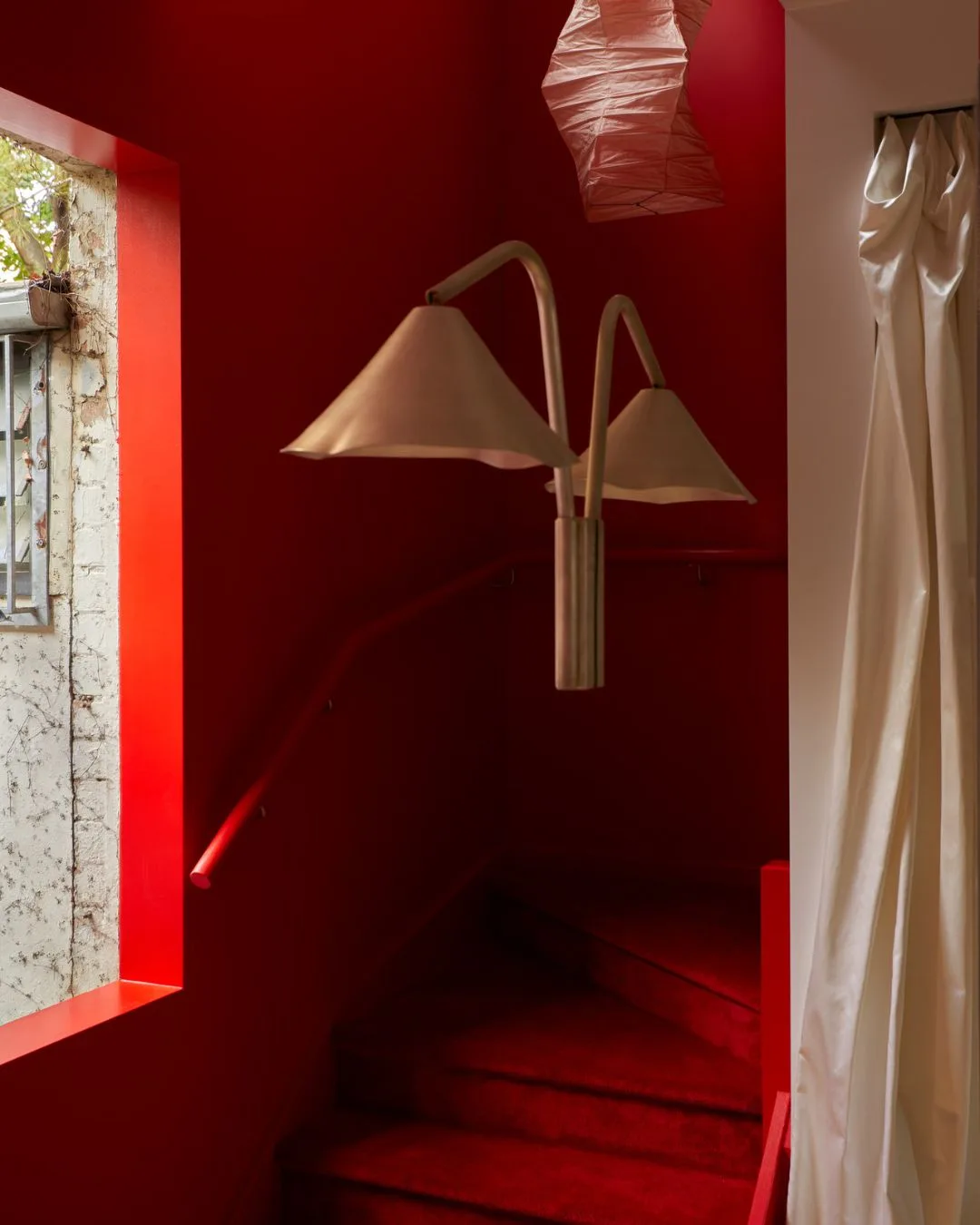A bold red staircase with red carpeted stairs and a designer wall sconce lighting with floral lampshade at the Henne Paddington Retail store