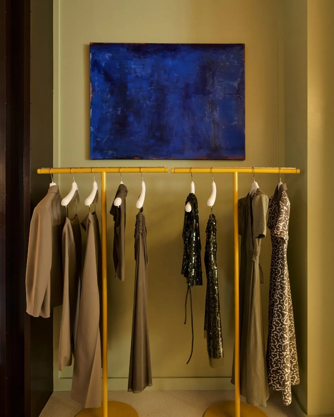 an olive green wall with a yellow clothing rack and blue artwork