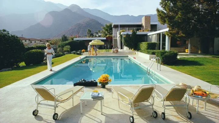 The pool of the Kaufmann house by Richard Neutra surrounded by yellow deck chairs and a view of the mountains in the distance.