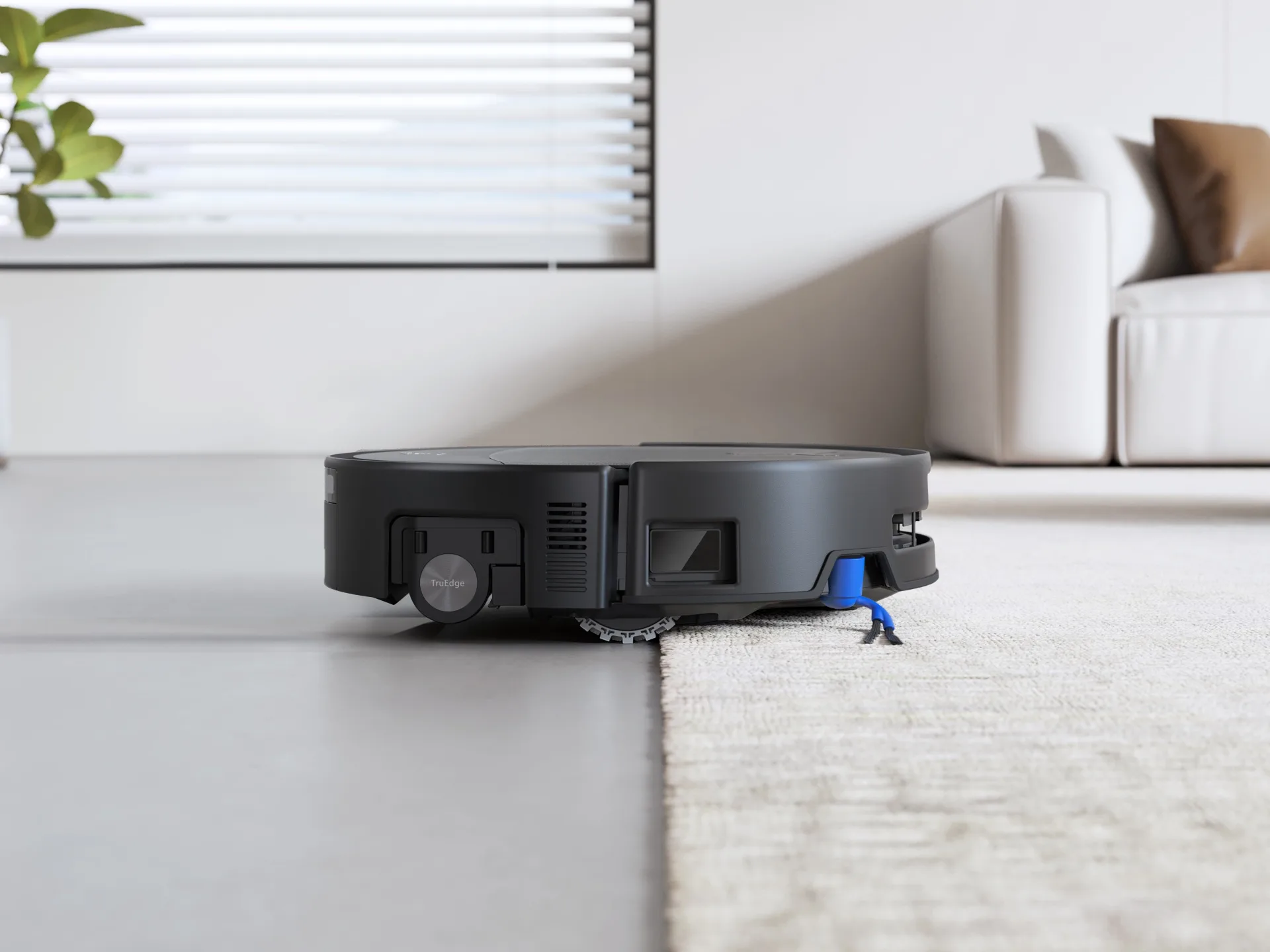 Robot vacuum cleaner moving from polished concrete flooring on to a rug. White couch in background.