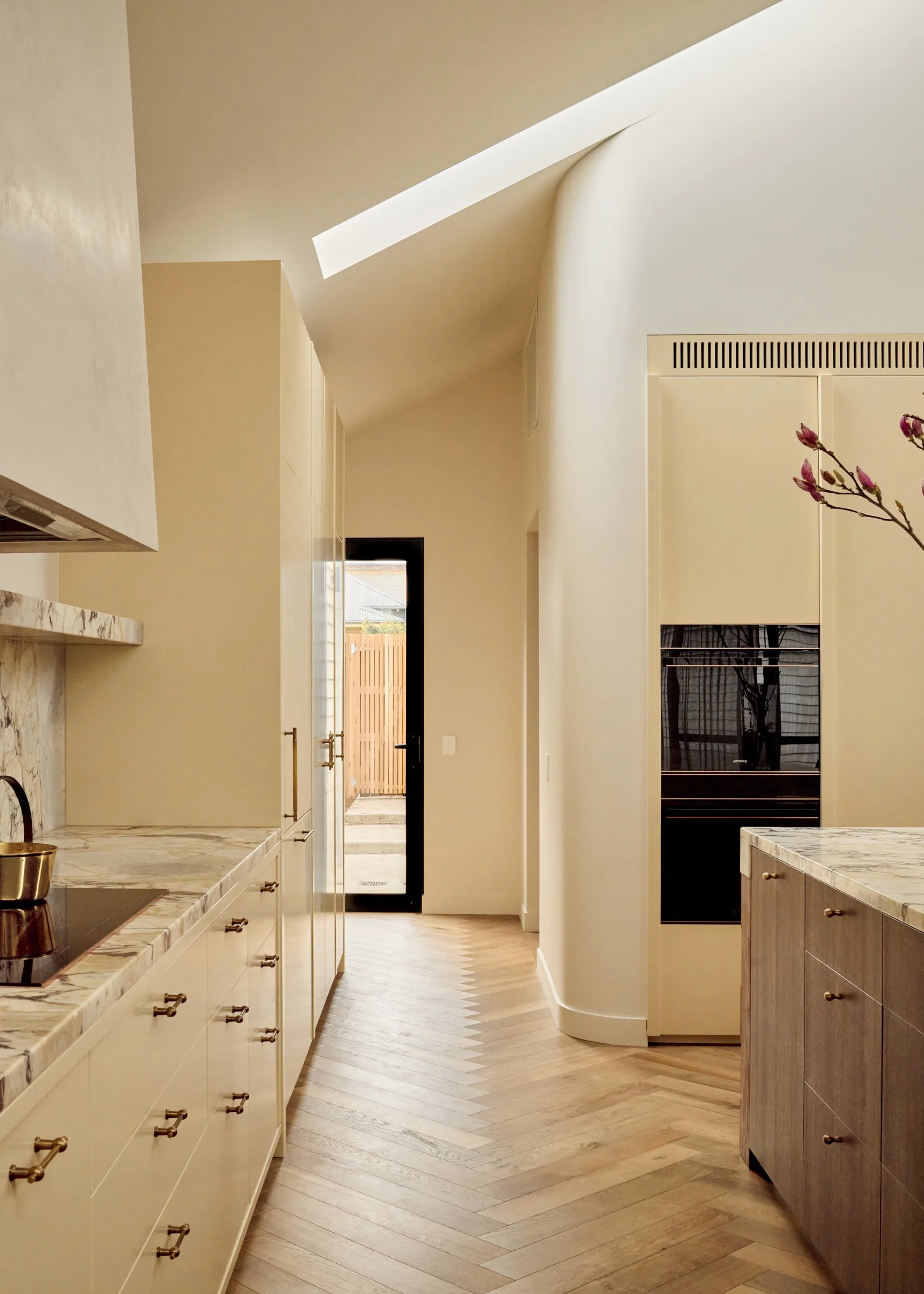 Contemporary kitchen with warm neutrals and earth tones, marble splashback, double oven, herringbone floors and a skylight.