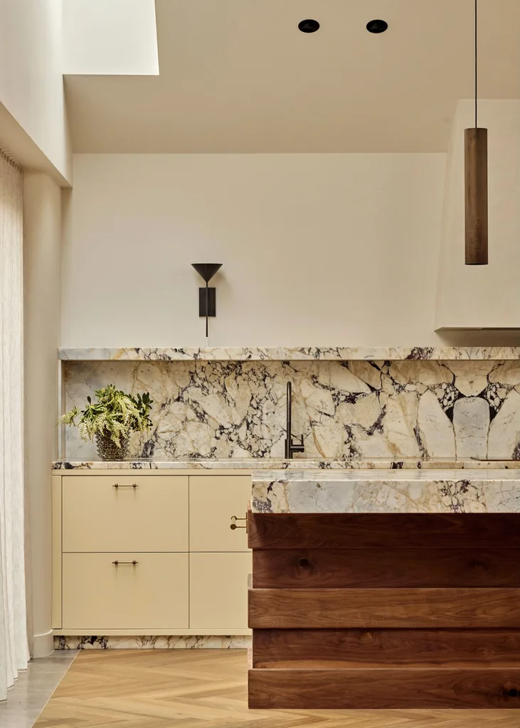 Contemporary kitchen with warm neutrals and earth tones, marble splashback, herringbone floors, a bronze sconce light and a timber island.