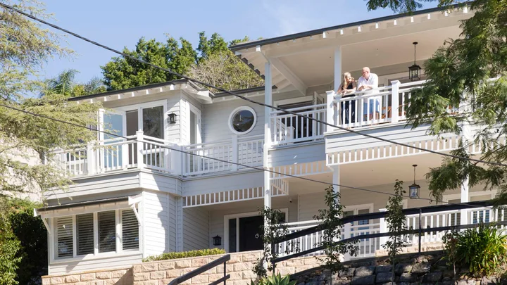 White two-storey coastal house with multiple balconies and verandahs with white slatted fencing