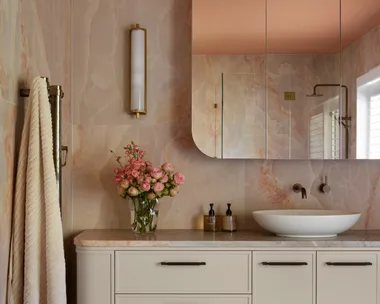 Luxurious bathroom with peach marble walls, floating vanity, vessel sink, floral arrangement, and checkered floor tiles in pinks and blues.