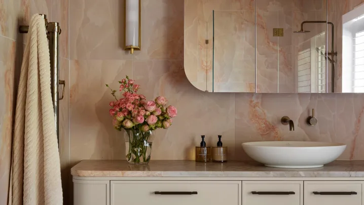 Luxurious bathroom with peach marble walls, floating vanity, vessel sink, floral arrangement, and checkered floor tiles in pinks and blues.