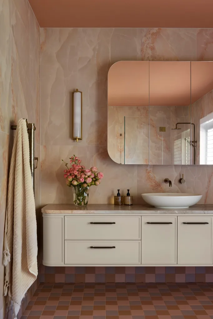 Luxurious bathroom with peach marble walls, floating vanity, vessel sink, floral arrangement, and checkered floor tiles in pinks and blues.