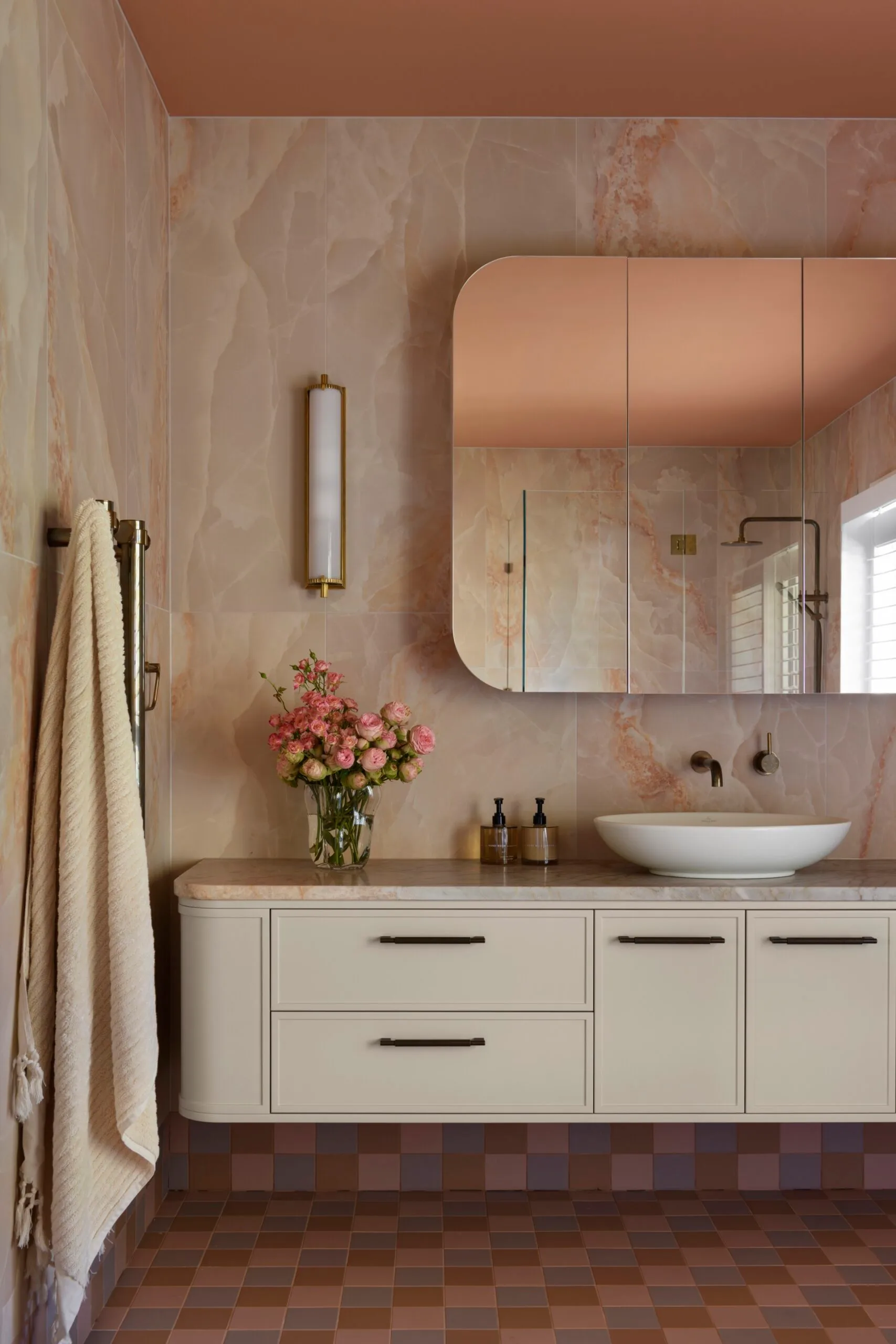 Luxurious bathroom with peach marble walls, floating vanity, vessel sink, floral arrangement, and checkered floor tiles in pinks and blues.