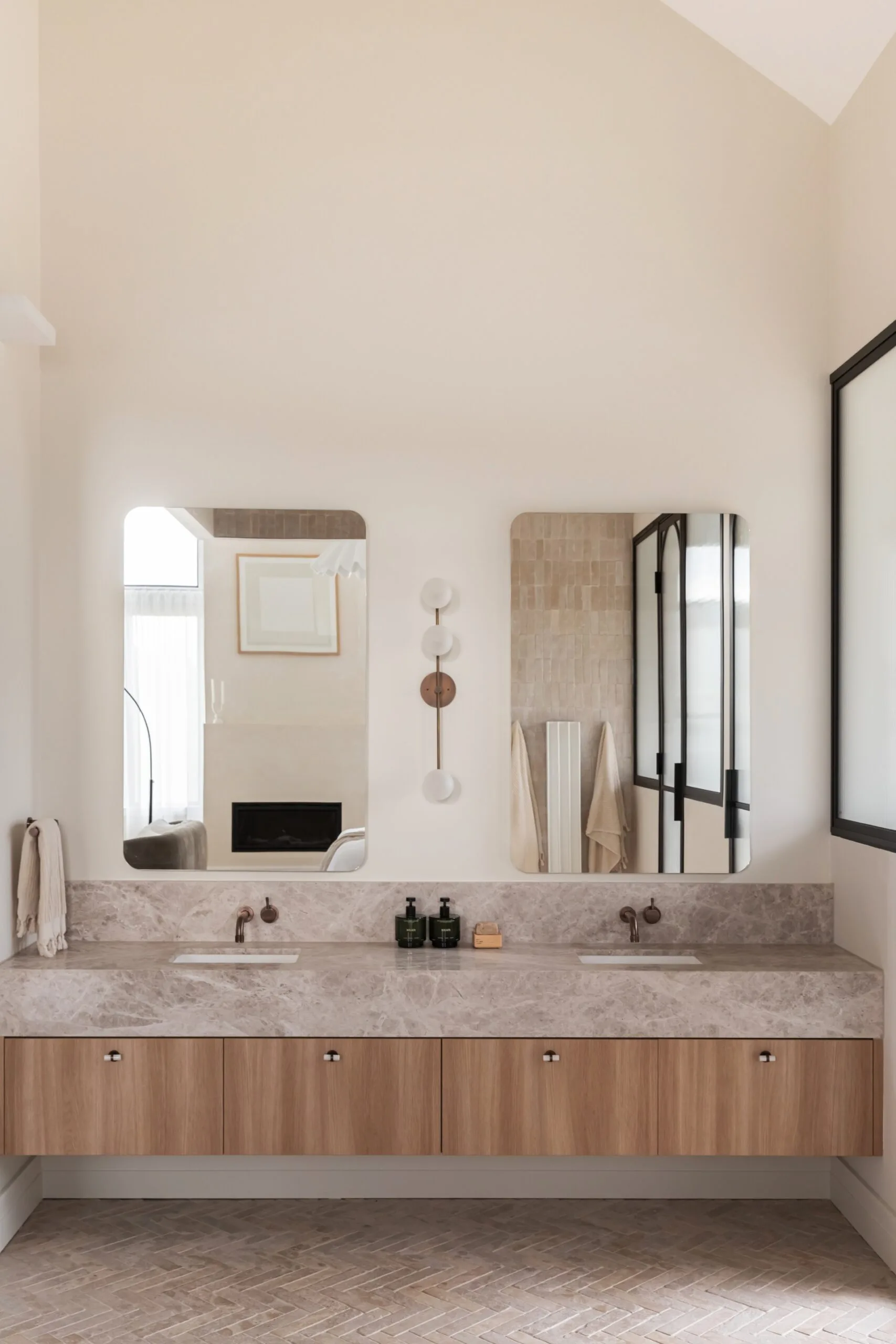 Dual-sink bathroom vanity with marble top, wooden cabinets, and large mirrors above, in a bright, modern setting.