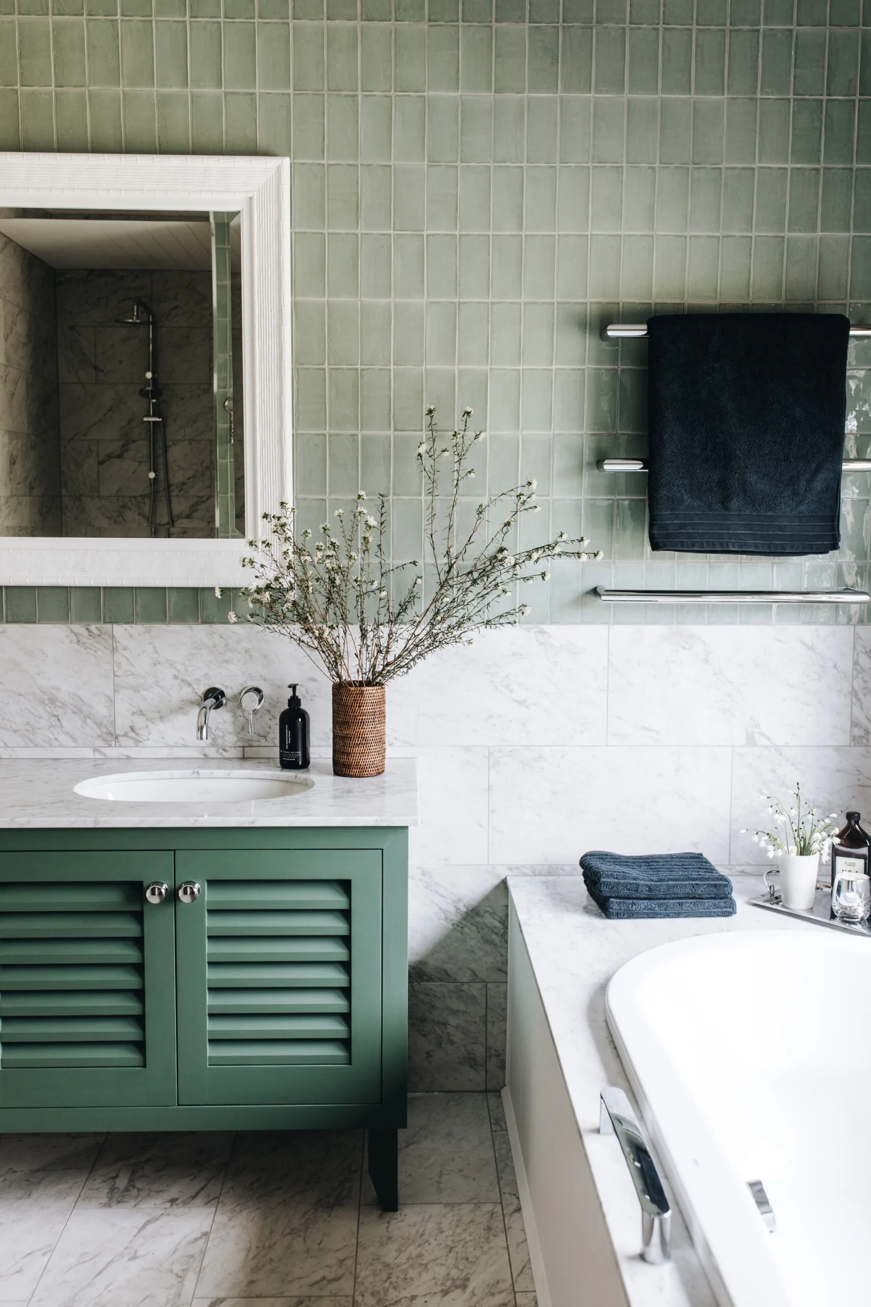 Elegant bathroom with green wall tiles, marble vanity countertop, and a built-in bathtub. The vanity joinery is also green.