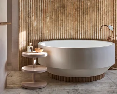 Luxurious bathroom with a large, round bathtub, textured fluted wall, and small round side table with soap and a bowl.