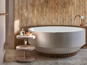 Luxurious bathroom with a large, round bathtub, textured fluted wall, and small round side table with soap and a bowl.