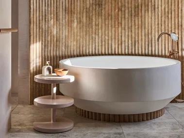 Luxurious bathroom with a large, round bathtub, textured fluted wall, and small round side table with soap and a bowl.