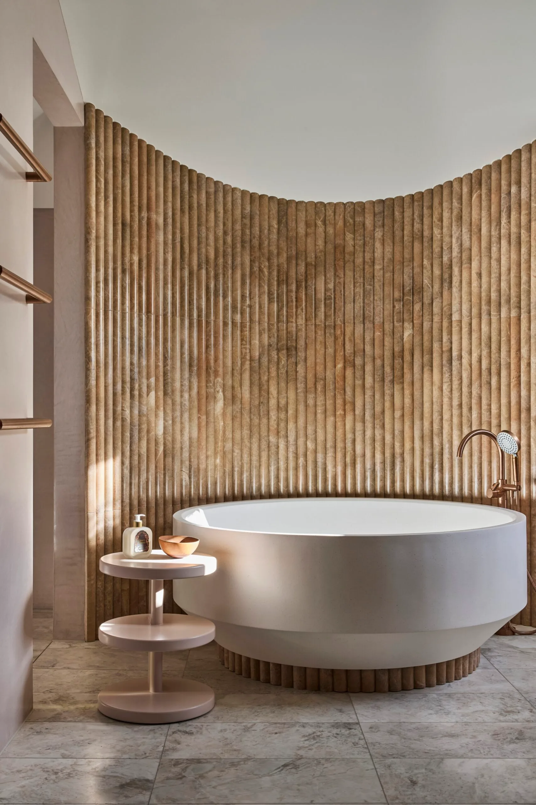 Luxurious bathroom with a large, round bathtub, textured fluted wall, and small round side table with soap and a bowl.