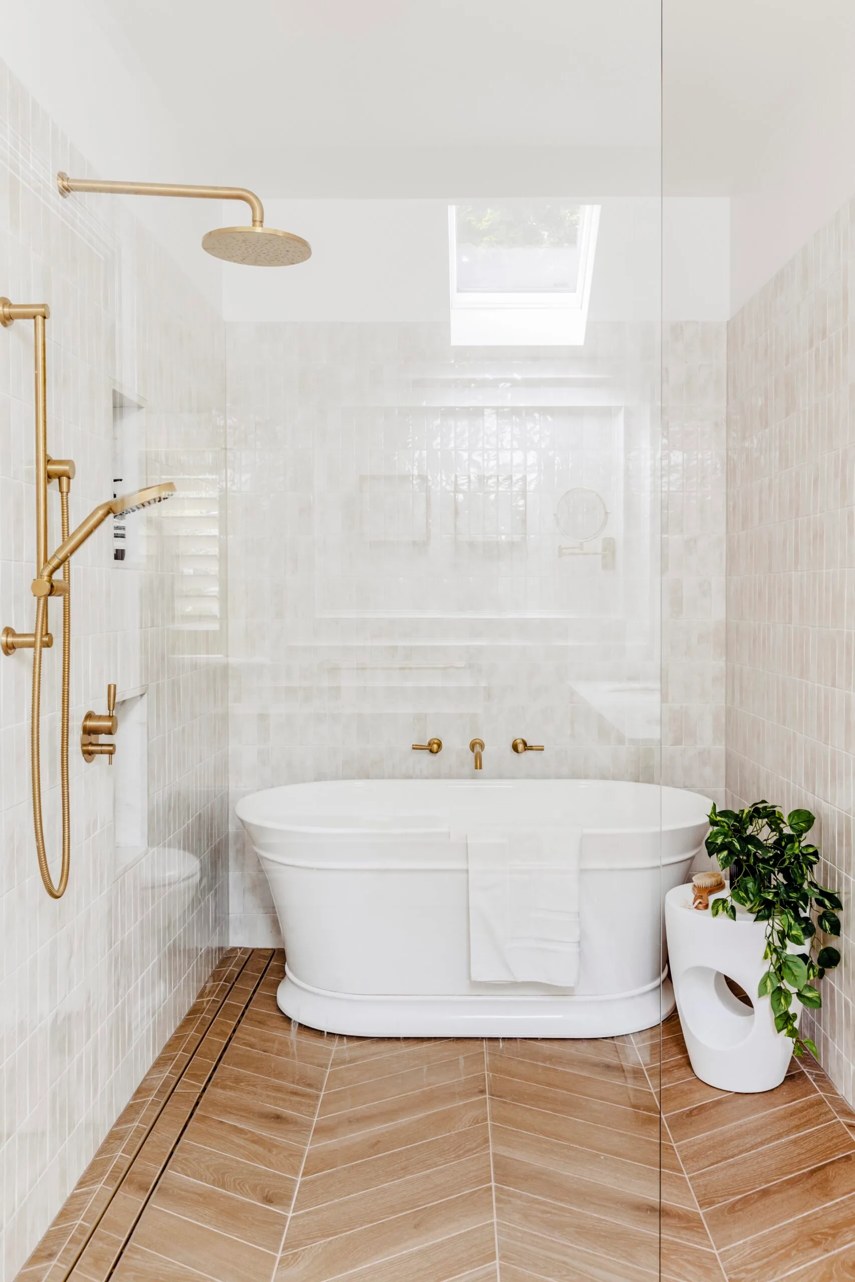 Luxurious bathroom with a white freestanding bathtub, gold tapware, timber floorboards, and a potted plant.