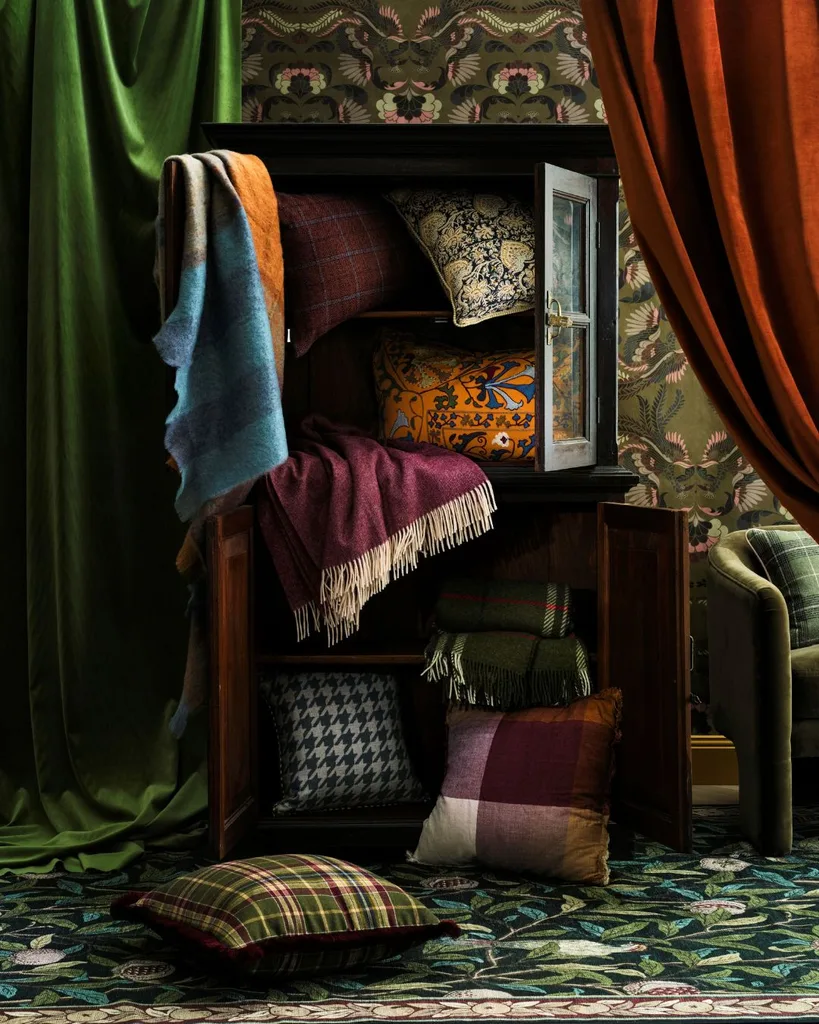 A rich coloured grand room with green velvet drapery and an antique wardrobe with wool blankets and cushions spilling out