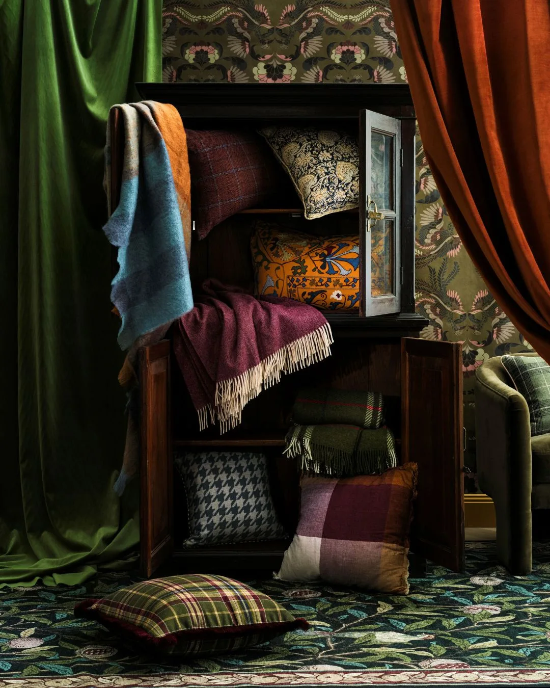 A rich coloured grand room with green velvet drapery and an antique wardrobe with  wool blankets and cushions spilling out