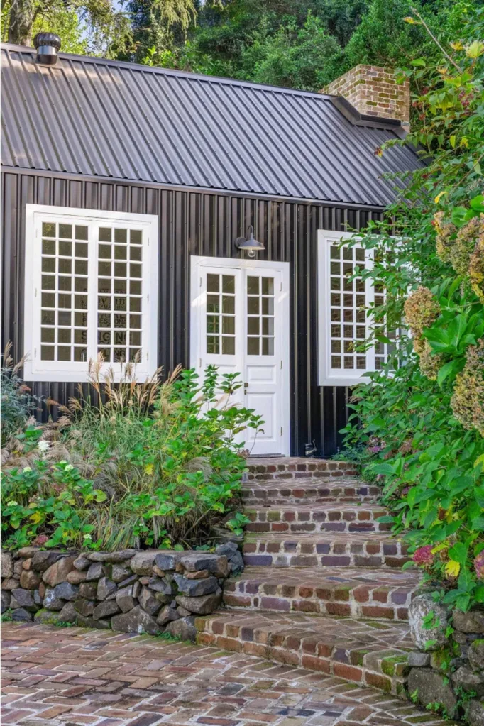 Recycled brick path to shed with chic dark exterior and white door and windows