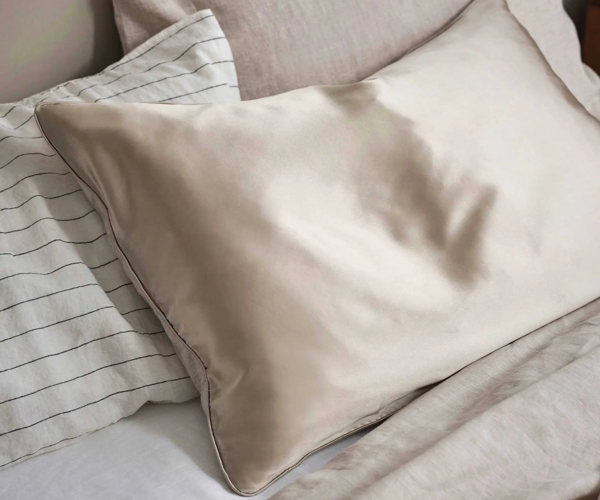Cultiver's Piped Silk Linen Flip Pillowcase in a natural, linen tone on a bed with striped linen bedding + split-material bedding and reversible silk and linen pillowcase