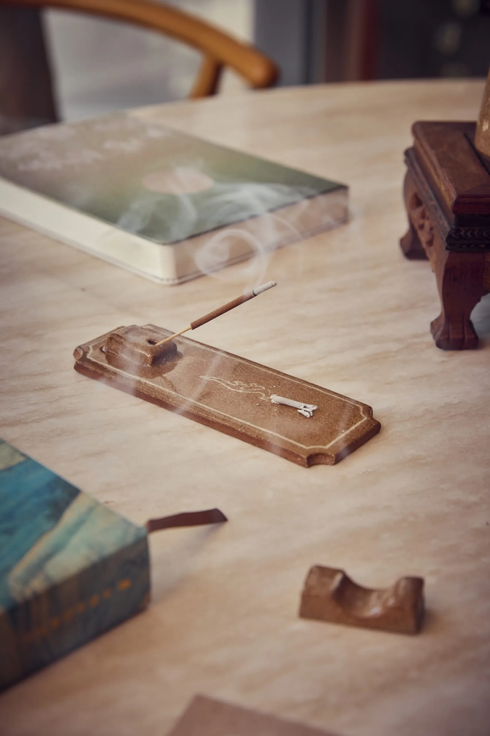 A close up photo of a handmade incense holder with incense in it. The incense is lit and smoke is curling up in the air. A notebook and chopstick holders are also in the image.